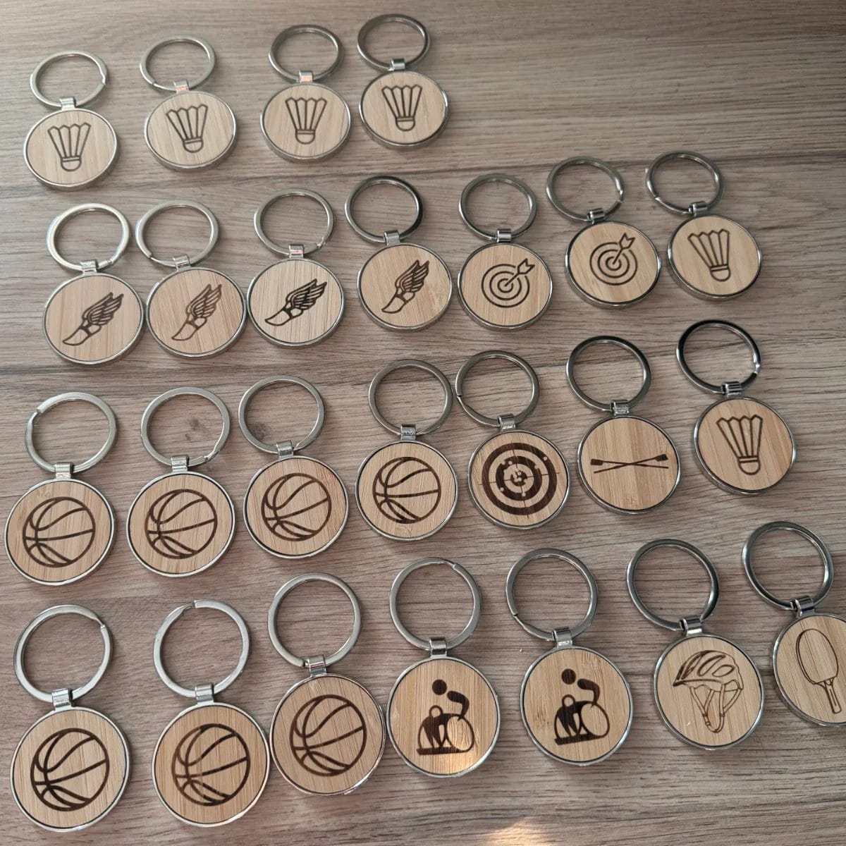 Edler Schlüsselanhänger Bambus rund mit gravierten Sport-Icons, ordentlich in Reihen auf hellem Holz angeordnet.