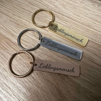 Drei Schlüsselanhänger "Chinaree" mit Wunschgravur liegen auf einer Holzoberfläche.