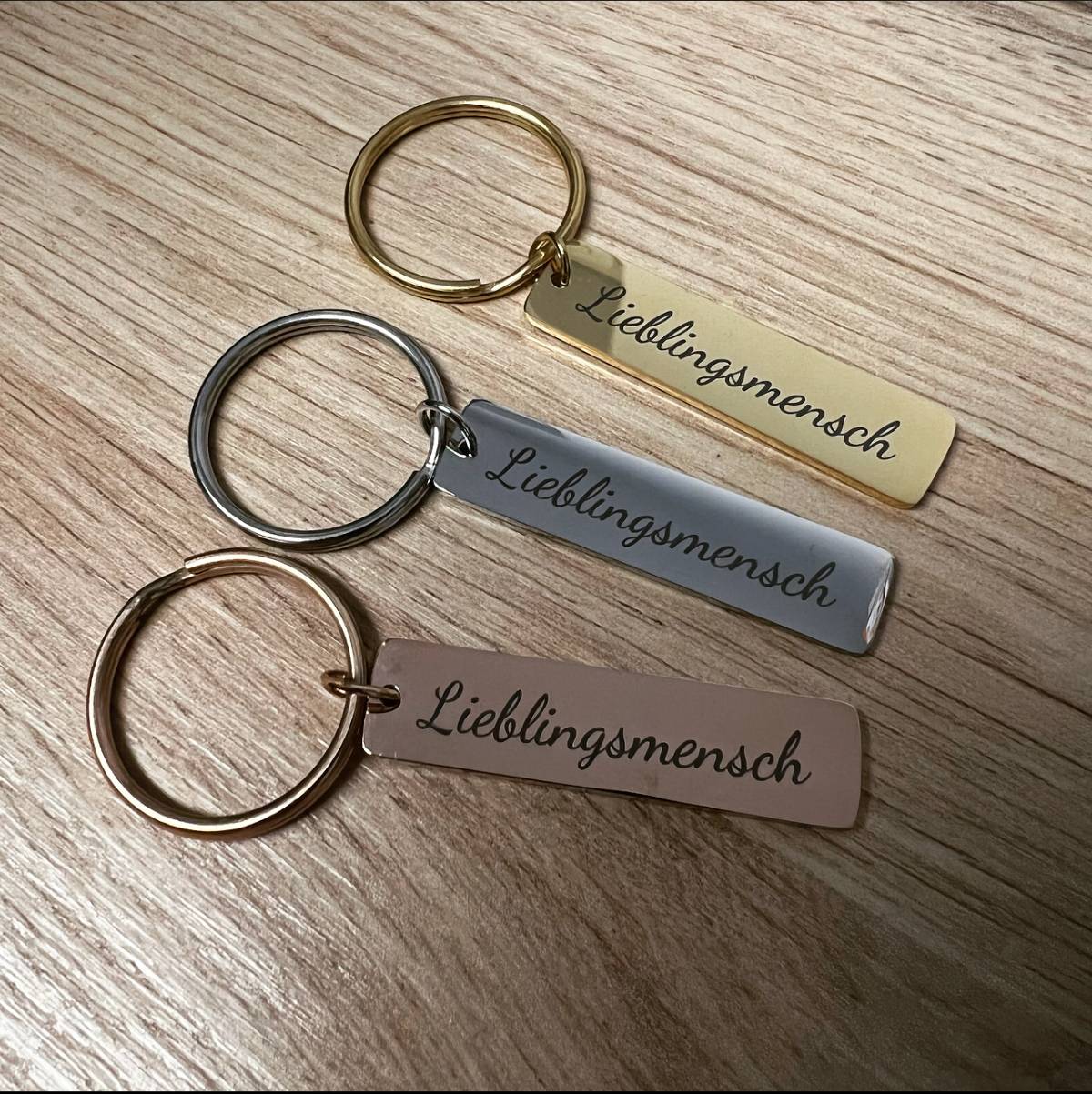 Drei Schlüsselanhänger "Chinaree" mit Wunschgravur liegen auf einer Holzoberfläche.