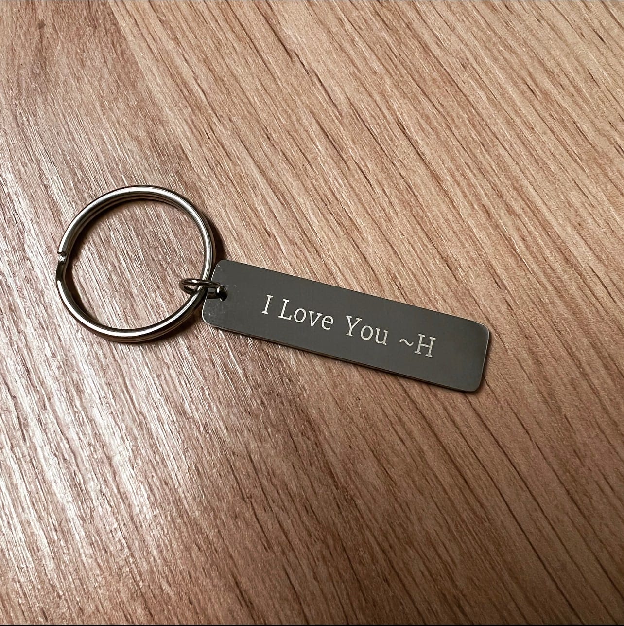 Der Schlüsselanhänger "Chinaree" mit Wunschgravur liegt aus Metall auf Holz, graviert mit "I Love You ~H".
