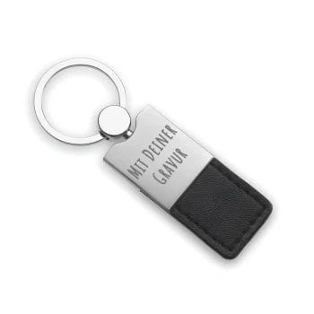 Ein Schlüsselanhänger aus Metall und schwarzem Leder mit der Gravur "MIT DEINER GRAVUR" auf dem Metallteil.